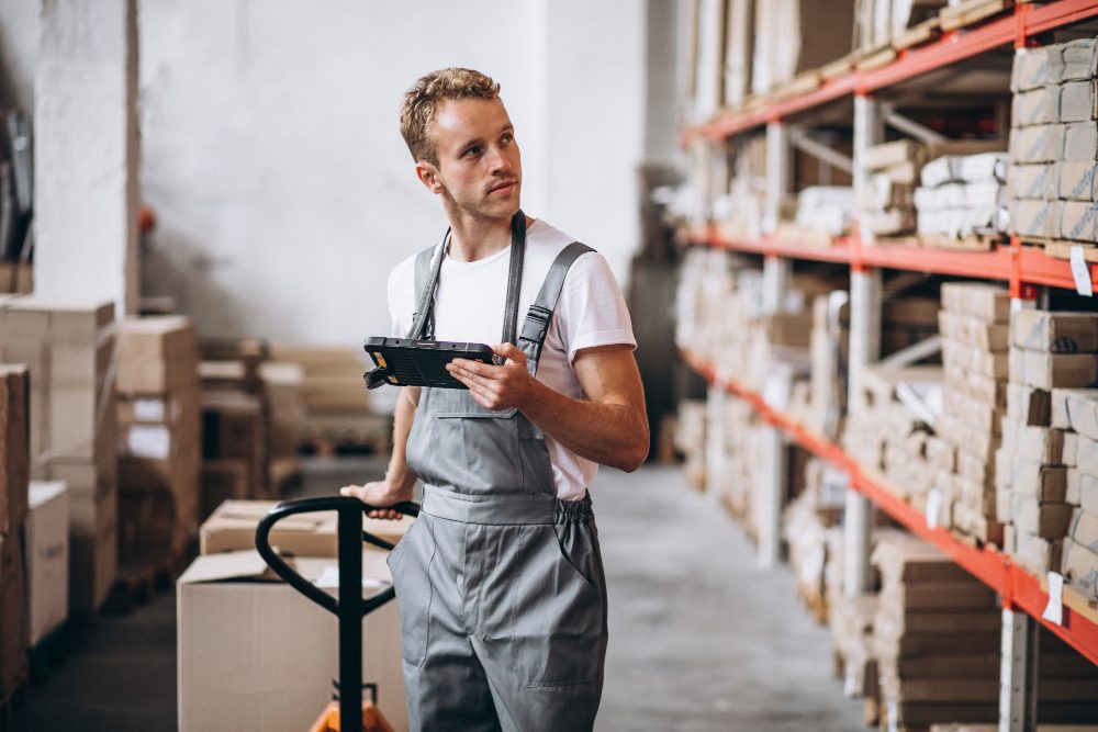 Man in warehouse using a tablet to take inventory and reduce warehouse costs